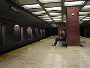 Una plataforma casi vacía de una estación subterránea de tren, con un hombre sentado en un banco