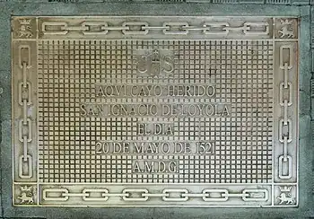 Placa conmemorativa situada en la acera delante de la puerta de acceso. A.M.D.G.