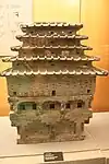 Modelo de cerámica de una torre de almacenamiento de granos de mediados de la época Han Occidental a principios del período Han Oriental con una pasarela en el primer piso con columnas, un balcón con columnas y techos de tejas de cinco capas apiladas una encima de la otra