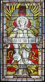La imagen en el vitral es de un ángel con sus alas estiradas detrás y sosteniendo una bandera que dice "Praice Ye the Lord" (Adorad al Señor)