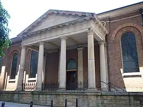 Columnas soportando el entablamento y el frontón extendiéndose de la iglesia para crear una entrada cubierta