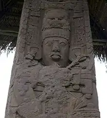 Primer plano de la parte superior de una estela labrada, que muestra el rostro de un rey con joyas y un tocado elaborado