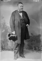 Grant is standing in a civilian dress suit holding a top hat.